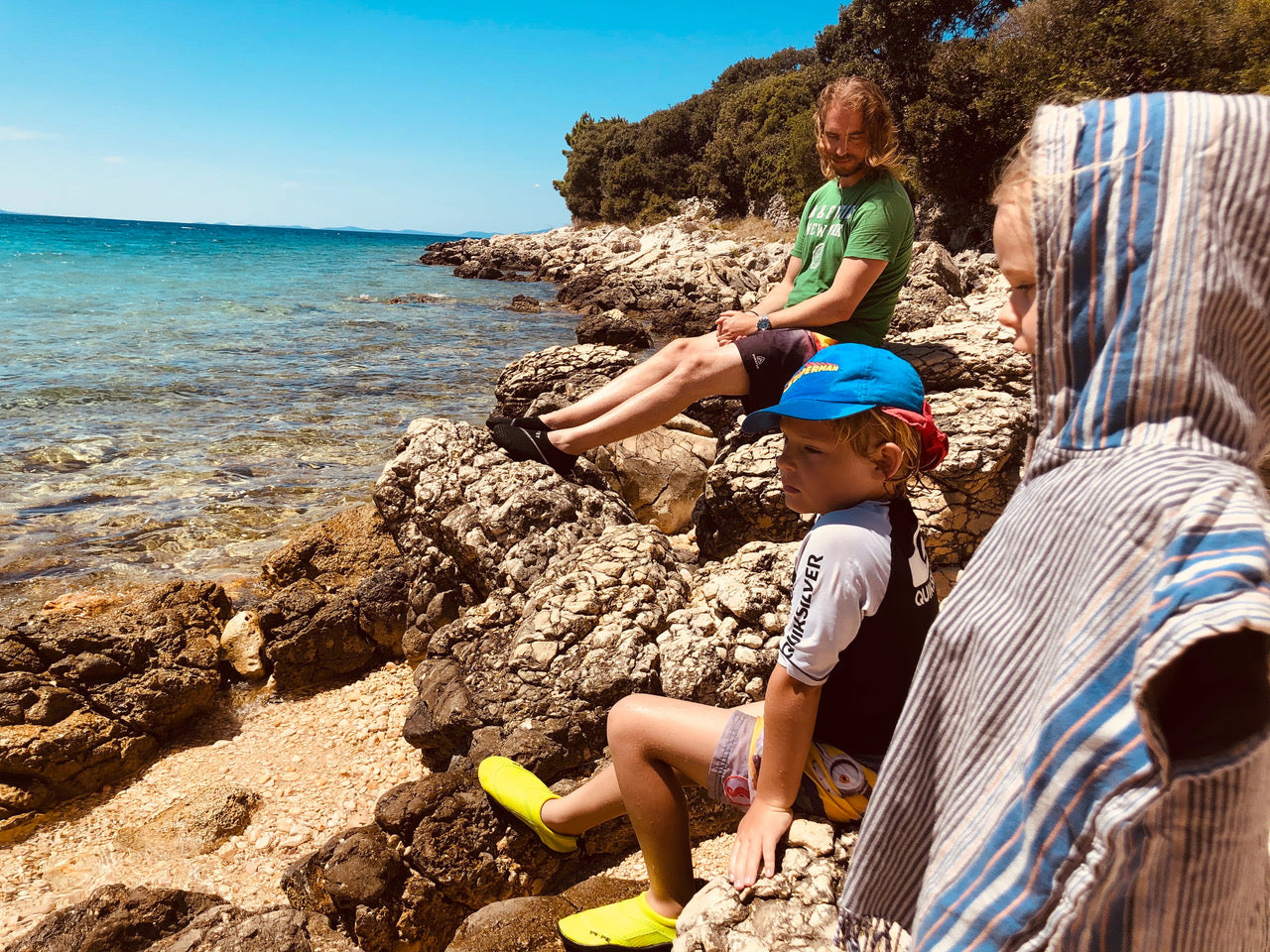 Familie (Papa, Sohn 10 Jahre, Tochter 7 Jahre) sitzt auf einem Felsen und schaut auf das wunderschöne, saubere Meer. 