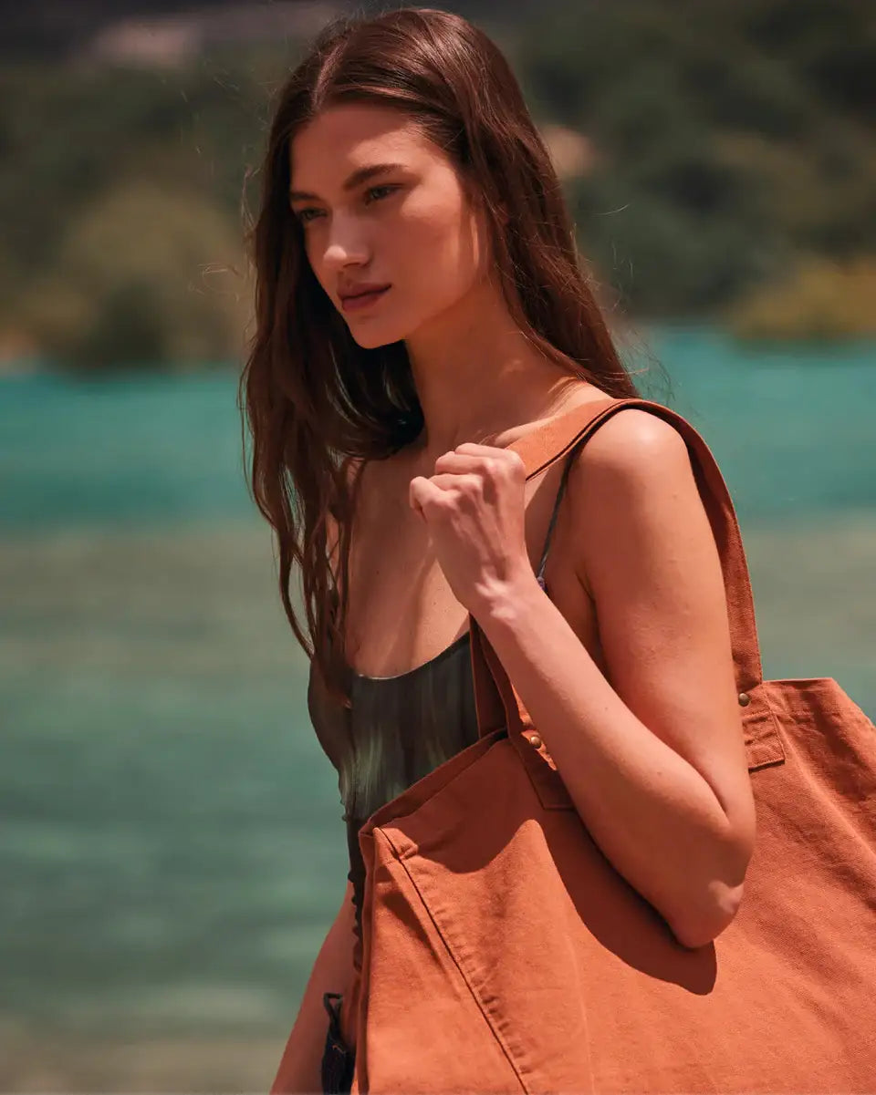 Junge Frau im Sommerkleid mit großen, rostfarbenen Stofftasche am Seeufer