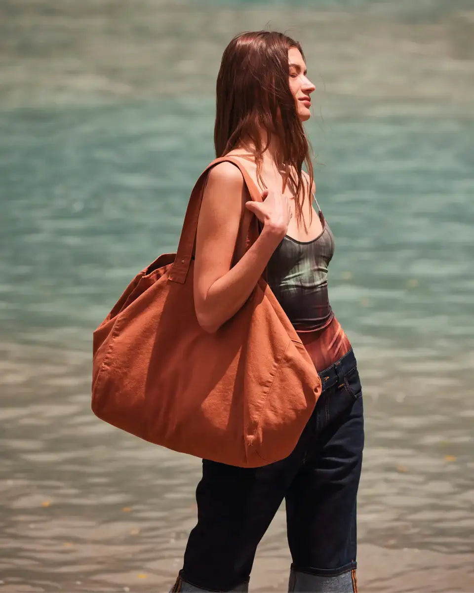 Frau am Wasser mit großer, brauner Stofftasche und lässiger Sommermode