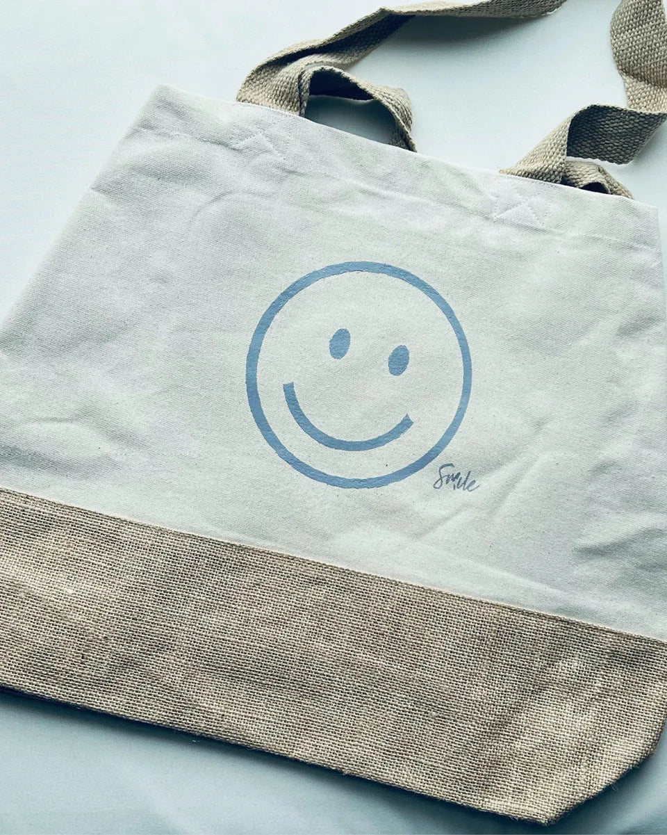 Nachhaltige Baumwoll-Jute Shoppingtasche mit blauem Smiley und Schriftzug Smile auf Naturstoff.