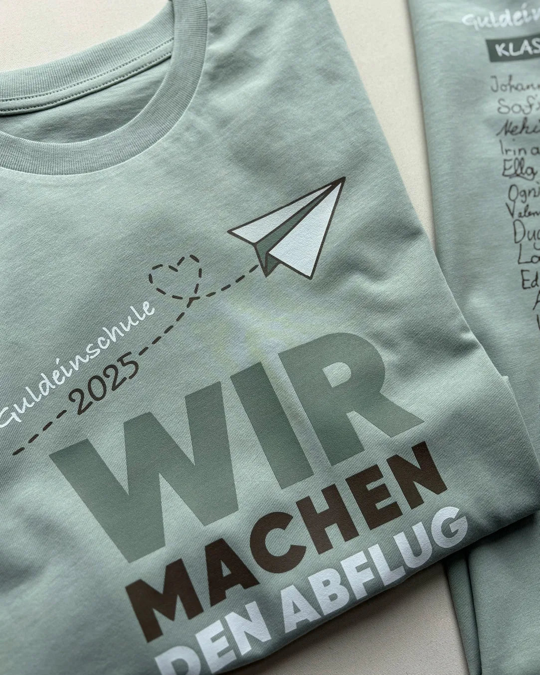 Grünes T-Shirt mit Aufdruck Papierflieger, Abschlussklasse 2025, Text Wir machen den Abflug