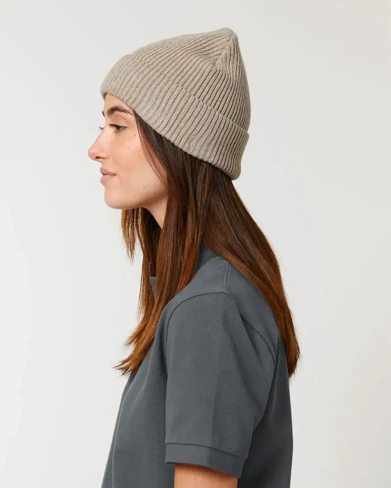 Frau mit beigefarbener Wollmütze im Profil, modernes Fischerbeanie-Design.