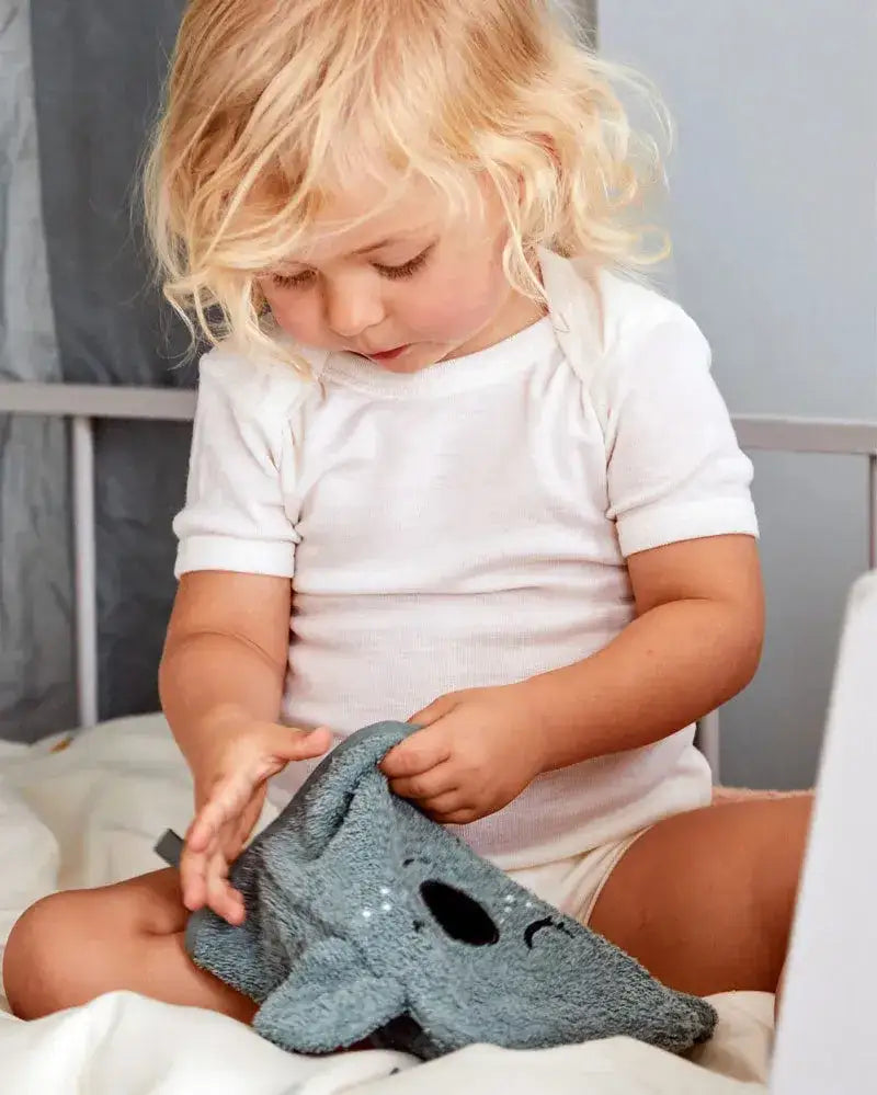 Kleines Kind spielt mit grauem Bio-Waschlappen in Koala-Form im Kinderzimmer