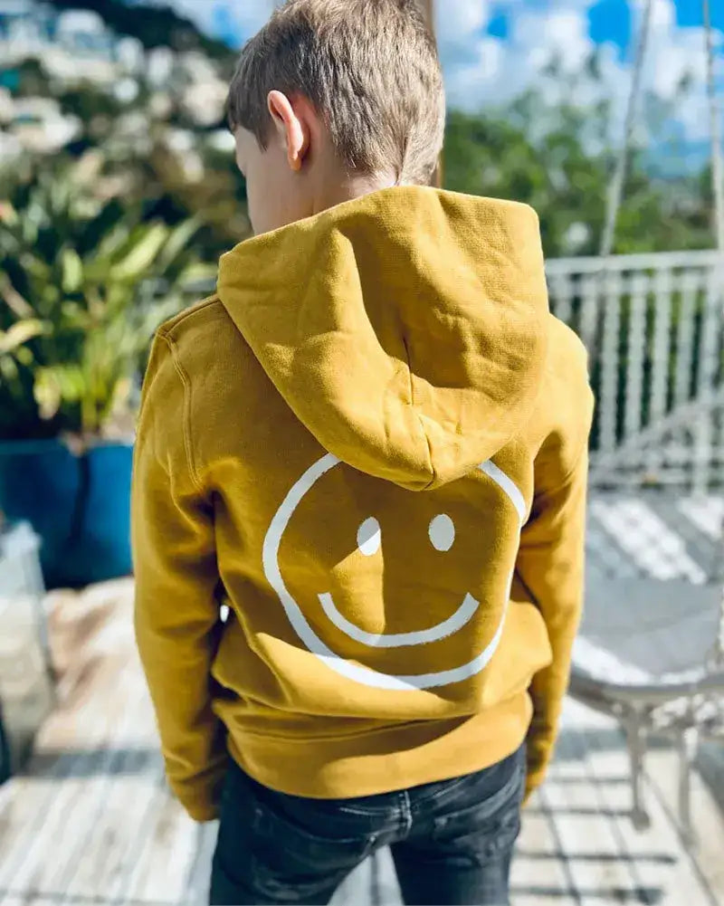 Kind in gelbem Hoodie mit großem Smiley-Aufdruck auf dem Rücken, draußen stehend