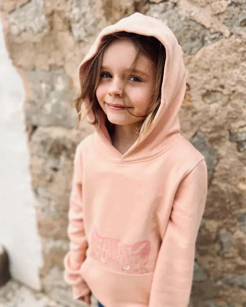 Mädchen im nachhaltigen, pfirsichfarbenen Bio-Kinder-Hoodie mit Leoparden-Motiv vor Steinwand