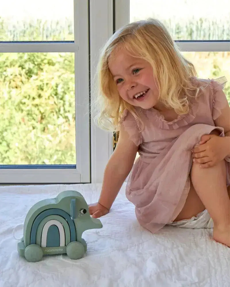 Lächelndes Mädchen spielt mit nachhaltigem Holz-Elefanten auf Rollen im Kinderzimmer.