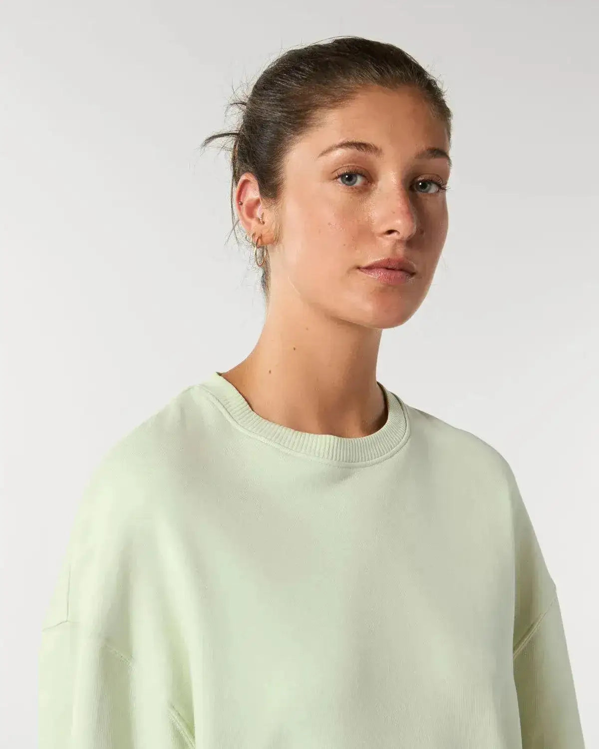 Frau trägt nachhaltigen, mintgrünen Oversize-Sweater vor hellem Hintergrund