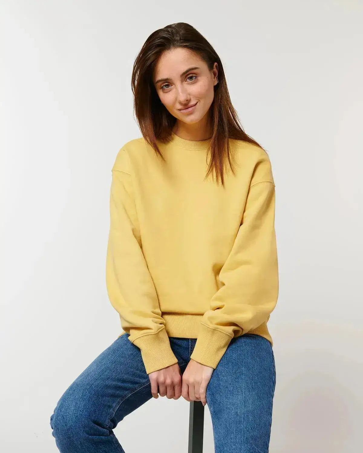 Frau in nachhaltigem gelbem Sweatshirt und blauer Jeans vor neutralem Hintergrund