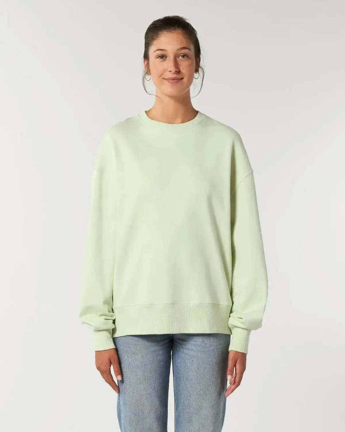 Frau trägt nachhaltigen, mintgrünen Oversize-Sweater und Jeans vor hellem Hintergrund