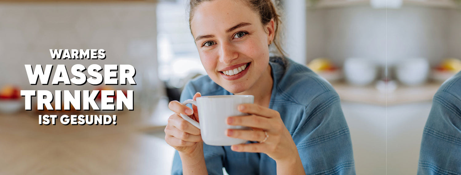 Junge Frau in heller Küche lächelt und hält eine Tasse warmes Wasser, Text: Warmes Wasser trinken ist gesund.
