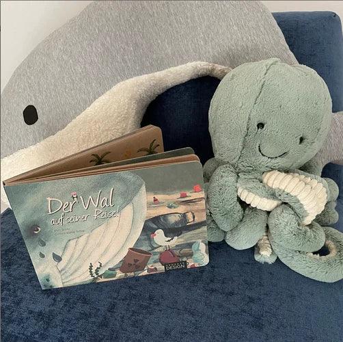Kinderbuch Der Wal auf seiner Reise neben Kuscheltier Oktopus auf blauem Sofa
