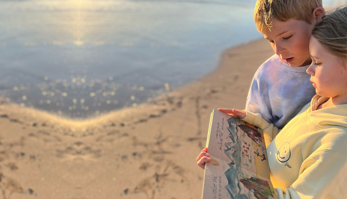 Junge und Mädchen stehen am Strand und schauen sich ein Buch über den Müll im Meer an.